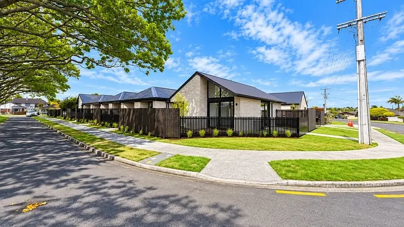 Corner view of 299 Levers Road, Matua, Tauranga, showing a brick home with raking gable glazing and dark slatted fencing