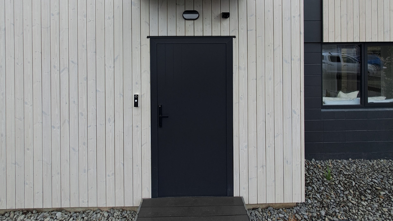 Black aluminium entrance door set within light vertical timber cladding at the 1 Manning Street development.
