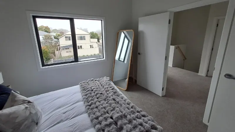 Upstairs bedroom with a black aluminium window, freestanding mirror and view towards the hallway.