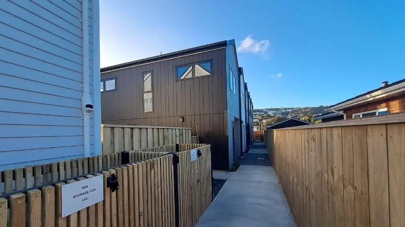 Shared pedestrian accessway between modern townhouses with timber fencing and dark-framed aluminium windows.