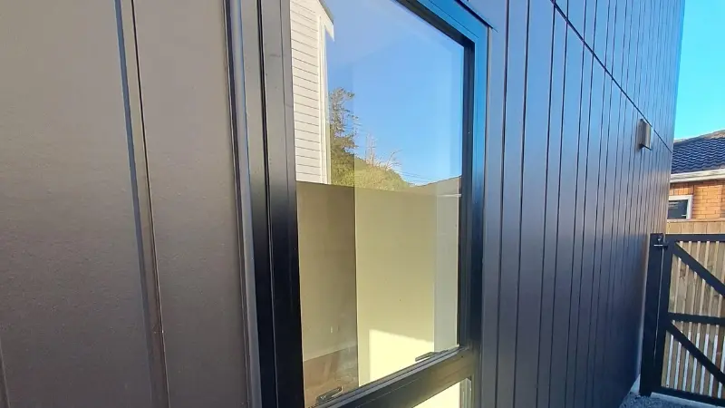 Close-up of a dark-framed aluminium window installed in the vertical cladding of a townhouse at 21 Derwent Street.