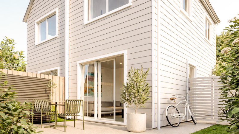 Private townhouse patio featuring an Appliance White aluminium stacker door, outdoor seating area, landscaped garden, and modern exterior cladding at ISOLA, Island Bay.
