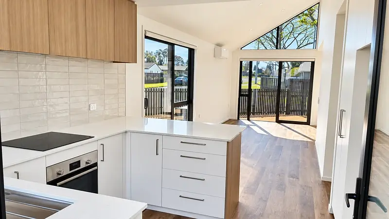 Open-plan kitchen and living area at 299 Levers Road, Matua, Tauranga, with a raked ceiling, gable glazing and aluminium doors to the deck