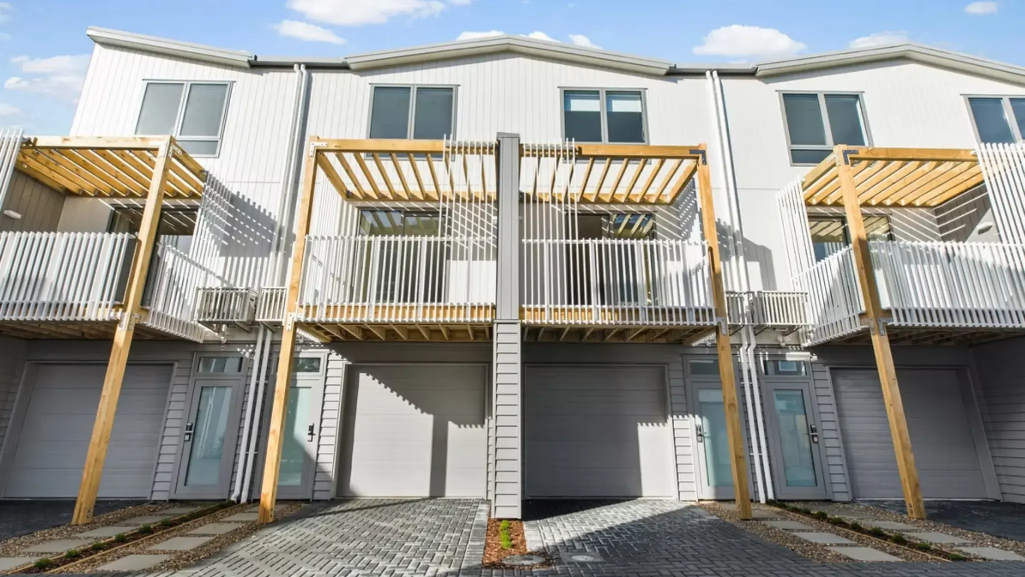 Rear view of multi-residential townhouses with balconies, aluminium windows, garage doors, and outdoor living spaces.
