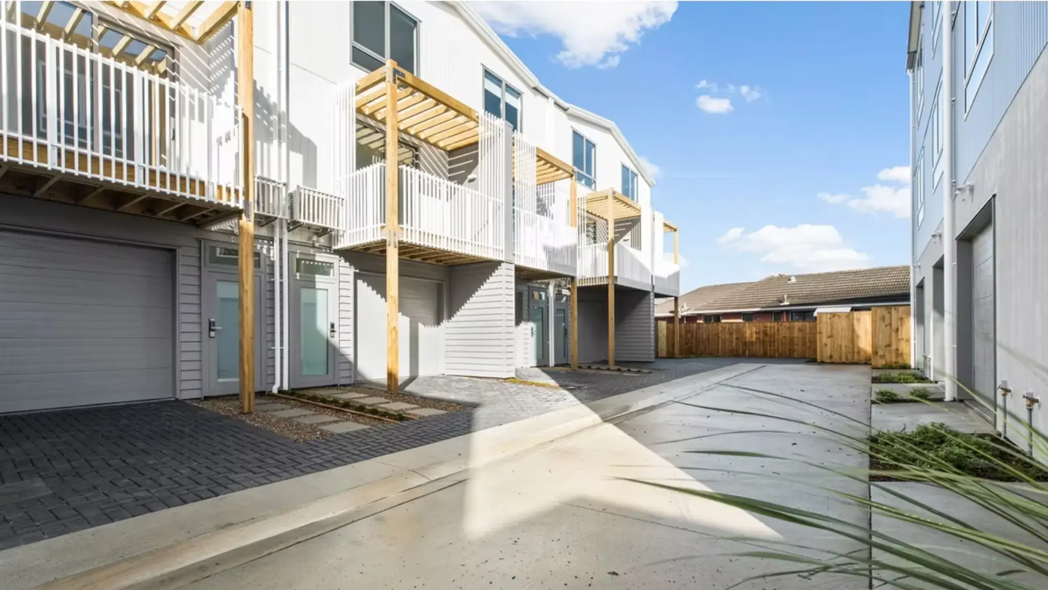 Shared driveway within a townhouse development featuring aluminium joinery, balconies, and landscaped surroundings.