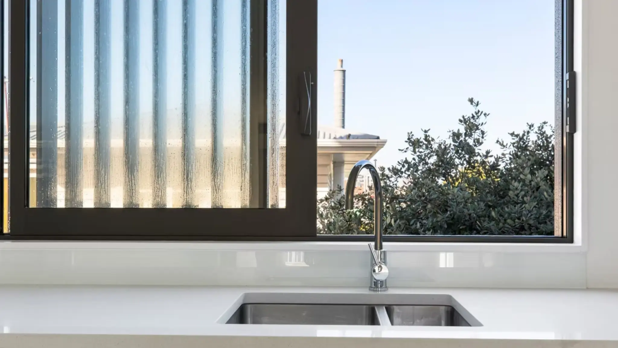 Close-up of a modern kitchen sink positioned beneath an aluminium awning window with textured privacy glazing.