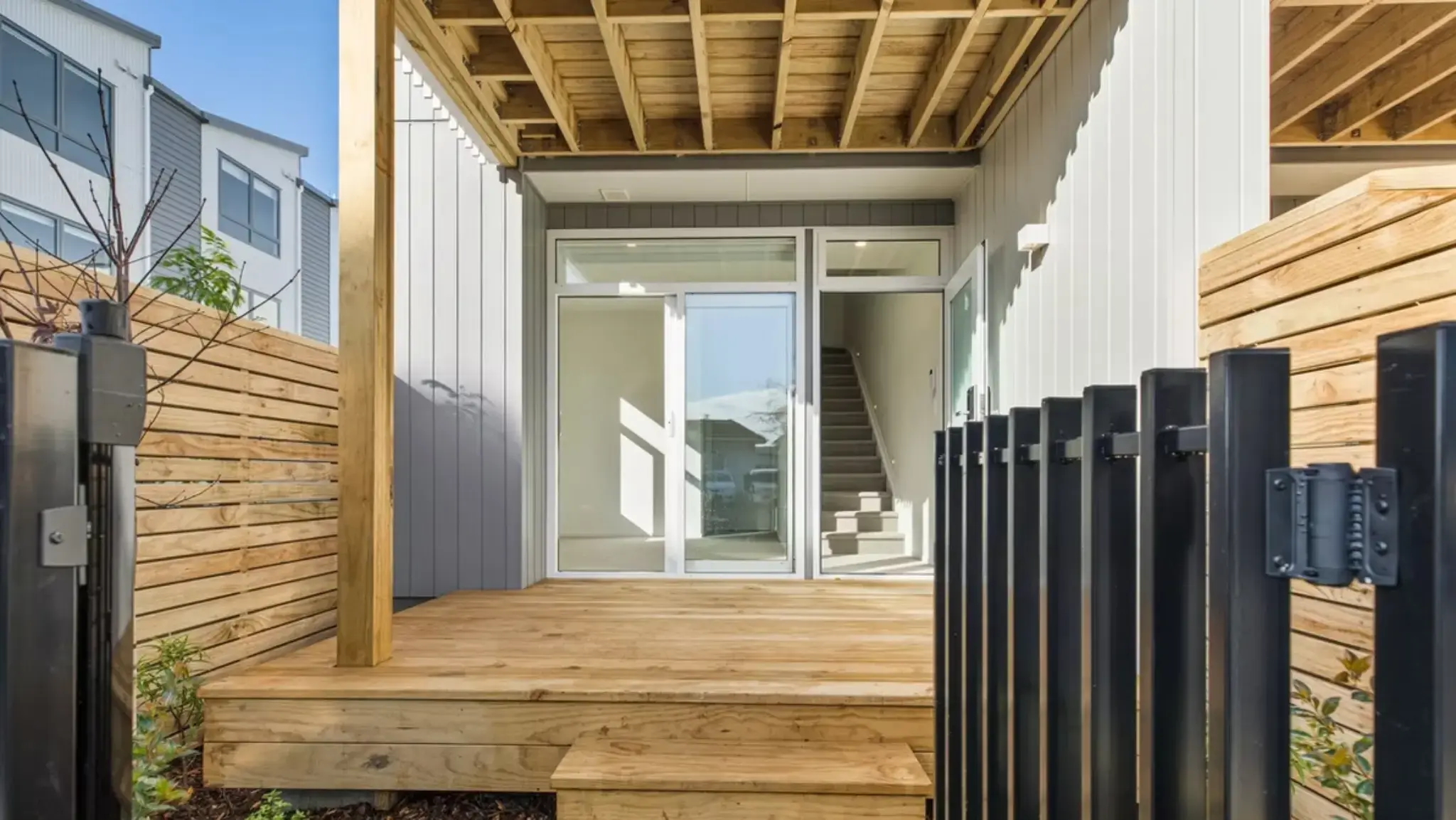 Private timber deck with aluminium sliding door and full-height glazed entry to a contemporary townhouse.