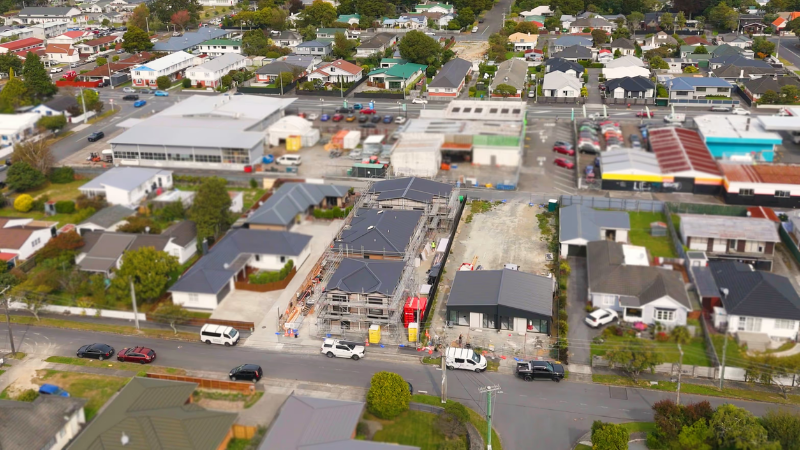 Aerial view of a residential construction site with multiple townhouse structures surrounded by suburban homes and streets.