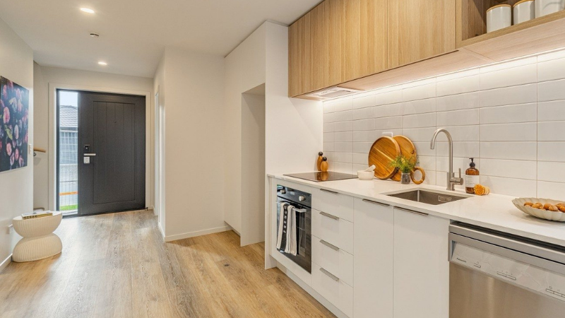 Modern townhouse kitchen with white cabinetry, timber cupboards, dark entrance door and timber-look flooring.