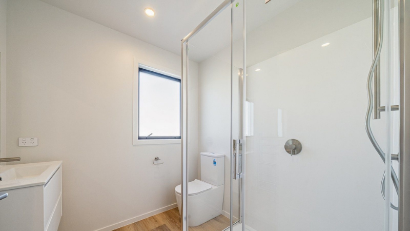 Compact modern bathroom with an aluminium awning window, glass shower, white vanity and toilet.