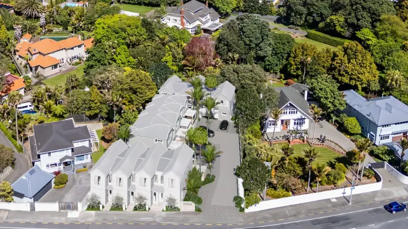 Aerial view of a townhouse development surrounded by mature trees, neighbouring homes, landscaped driveways, and tropical planting.