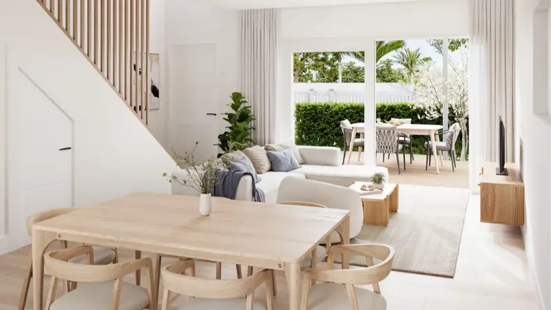 Bright modern living and dining space with timber staircase, neutral furnishings, and large sliding doors opening to an outdoor patio.
