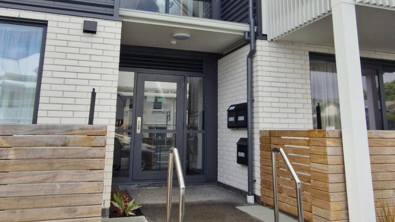 Apartment entrance with aluminium commercial hinged door and glazing in Matt Grey Friars, New Plymouth multi residential project