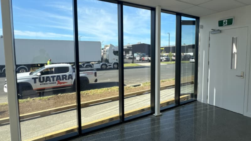Interior commercial space with full-height aluminium windows overlooking street and industrial surroundings.