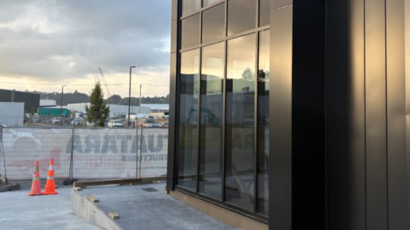 Corner detail of commercial aluminium glazing system with vertical cladding and reflective glass panels.