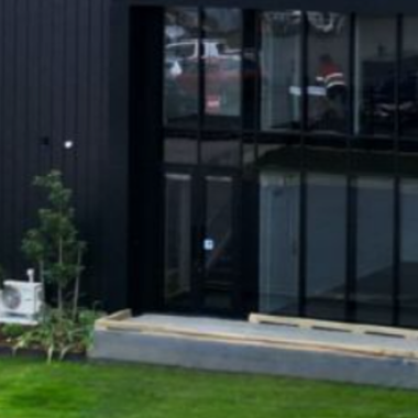 Black aluminium entry door with full-height glazed panels in a multi-residential building, featuring modern landscaping and concrete entry.