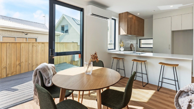 Open-plan dining and kitchen area featuring aluminium sliding doors opening onto a private outdoor deck at St Giles Park View, Wellington.