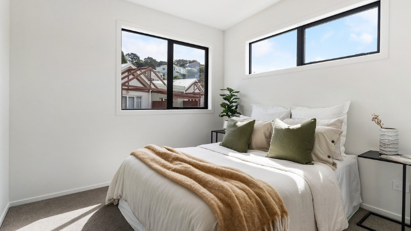 Bright bedroom with large aluminium windows providing natural light and views across the surrounding Kilbirnie neighbourhood.