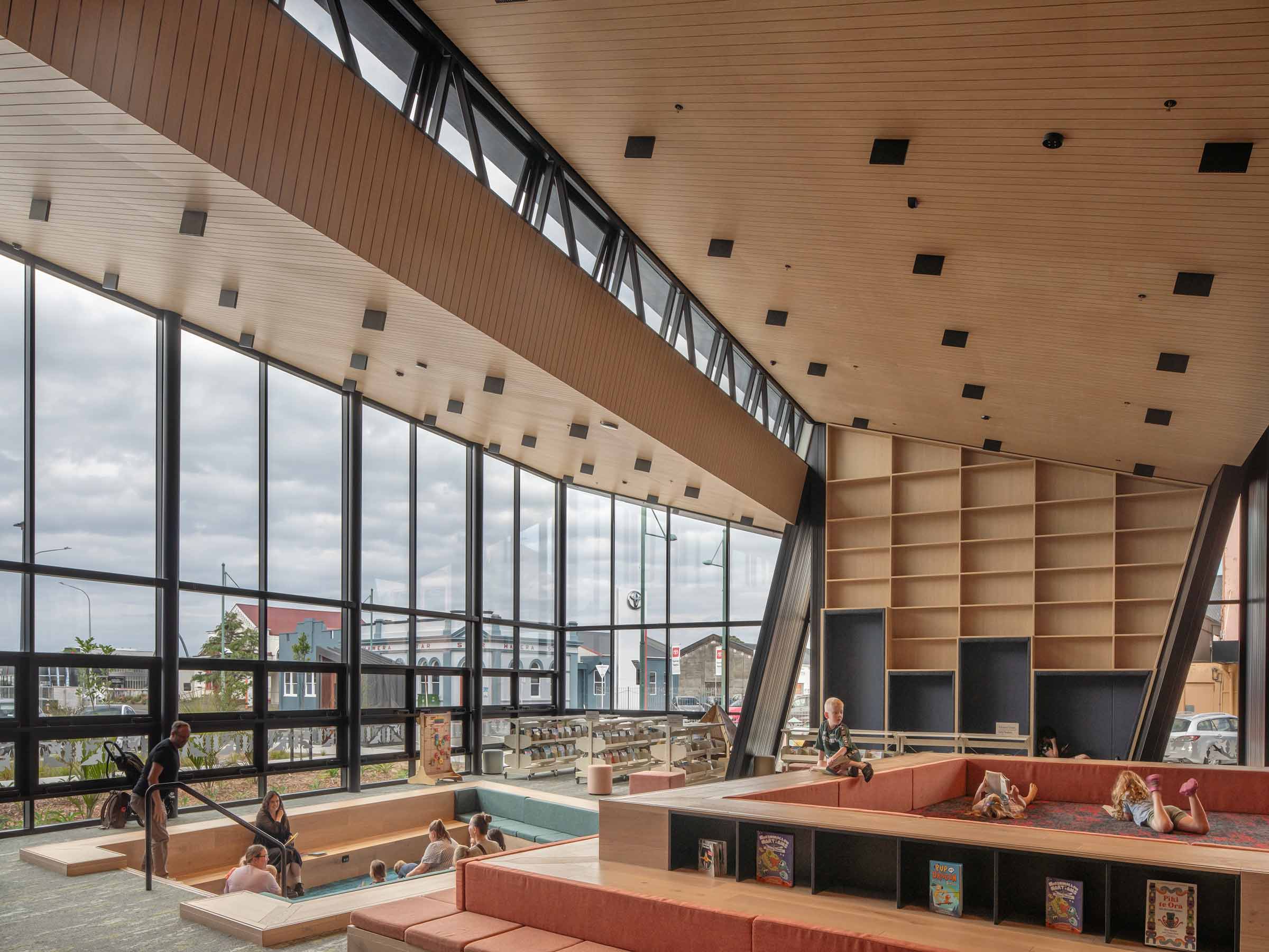 Interior of Te Ramanui o Ruapūtahanga library with children’s reading area, large floor-to-ceiling windows, and timber ceiling panels filling the space with natural light.