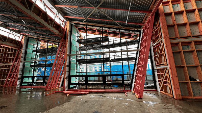 Under-construction interior of Te Ramanui o Ruapūtahanga showing aluminium window framing installed within angled timber structures and scaffolding in place.