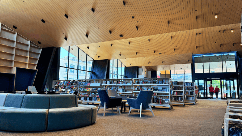 Wide-angle interior shot of the library space at Te Ramanui o Ruapūtahanga, featuring UNO aluminium joinery, expansive glazing, and warm timber finishes with soft seating and book displays.